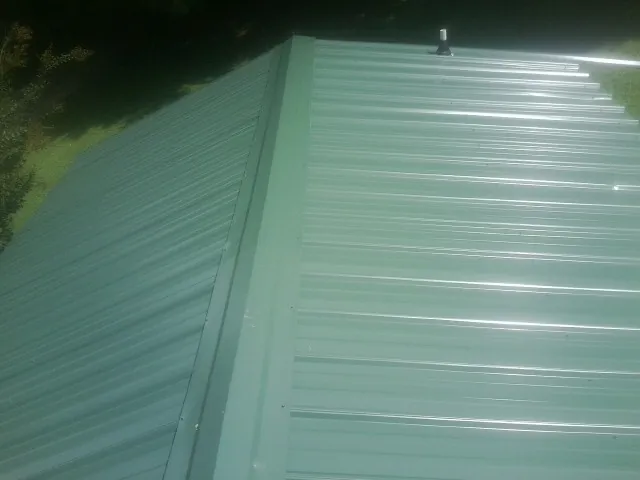 New green metal panels meeting at the ridge of a roof — Flat Roof Repair work by our crew in Florence